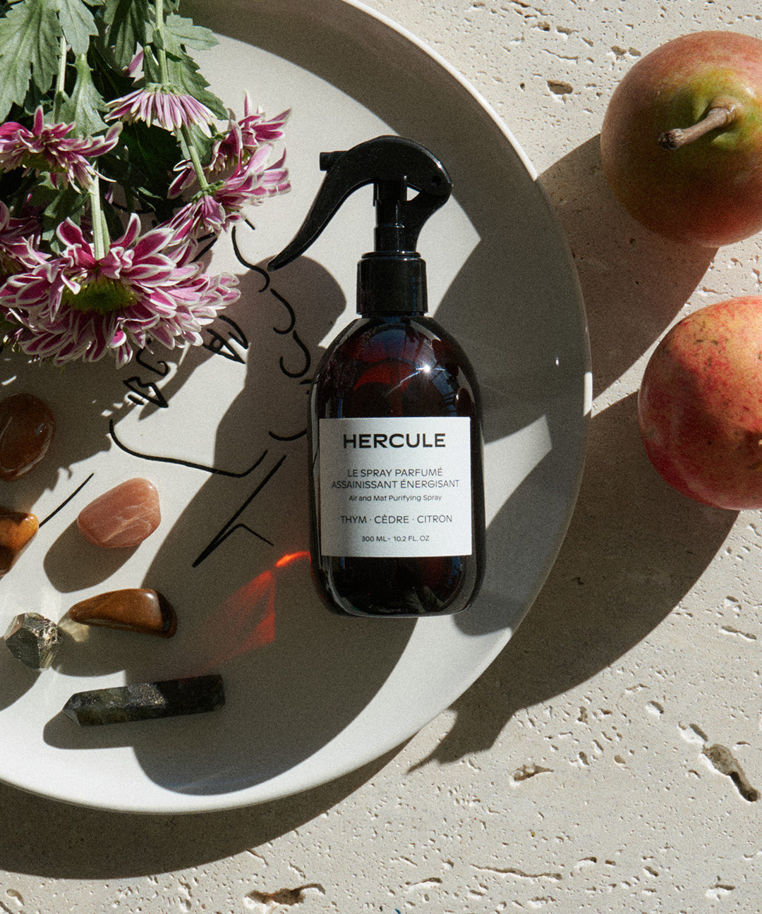 Spray pour assainir le tapis de sport et énergiser l'espace d'entraînement photo du produit sur une assiette et disposition de fleurs et pierres 