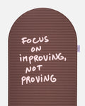 Close-up on the pink quote “focus on improving not proving” on the Hercule Studio x Thomas Lélu sport mat, artistic message and graphic typography
