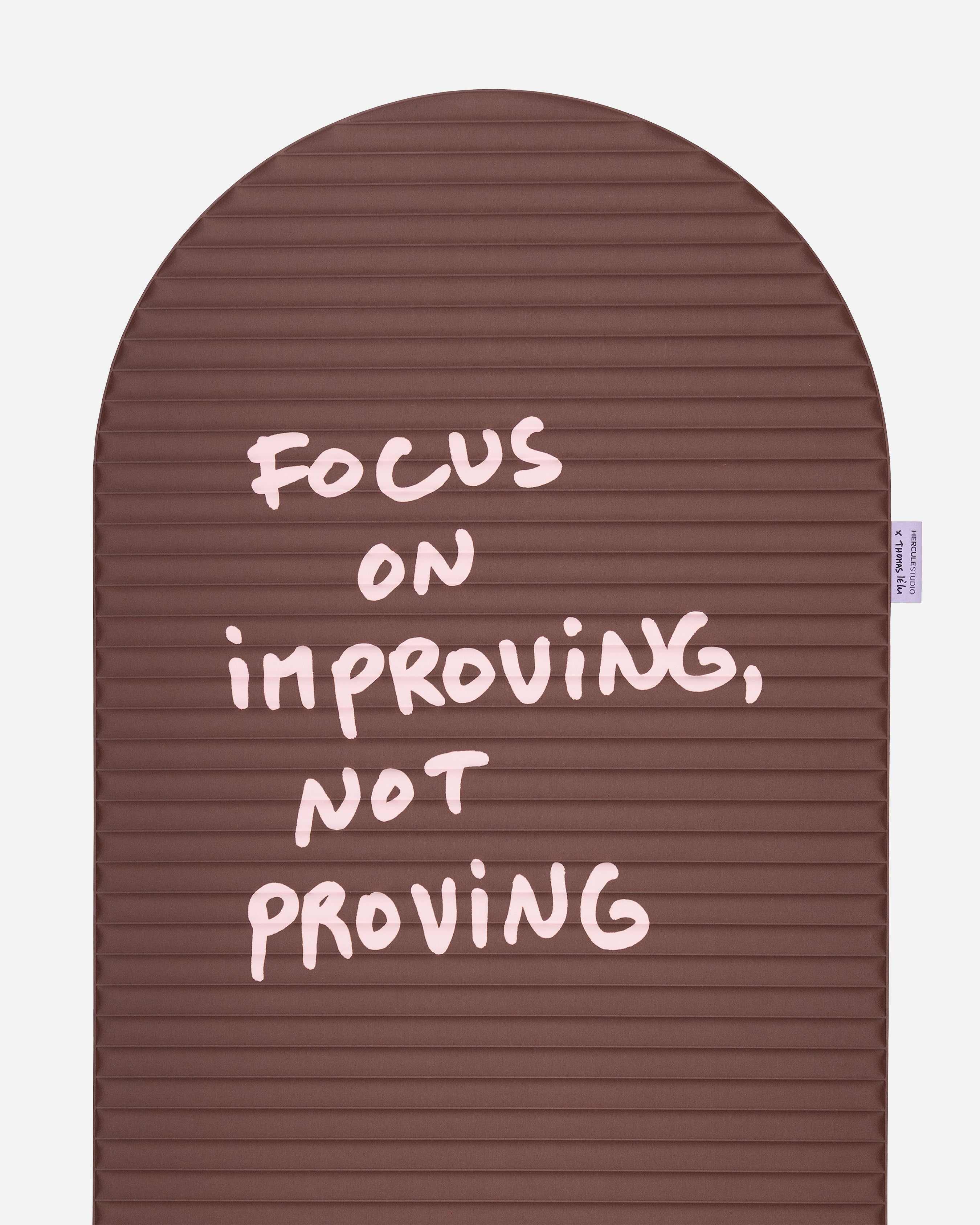 Close-up on the pink quote “focus on improving not proving” on the Hercule Studio x Thomas Lélu sport mat, artistic message and graphic typography