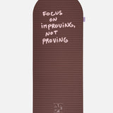 Hercule Studio x Thomas Lélu Limited Edition Exercise Mat, brown designer floor mat featuring a pink quote reading “focus on improving not proving,” an artistic collaboration for fitness, Pilates, and stretching, unfolded view